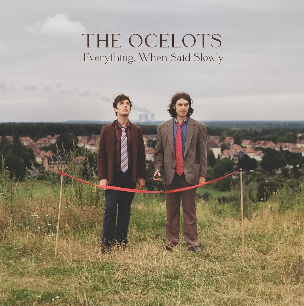 Everything When Said Slowly cover: The Ocelots standing in suits in a grassy field with a red ribbon between them.